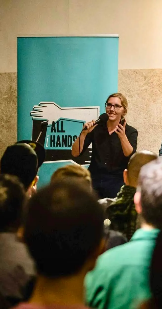 Claudia speaking into a microphone in front of an All Hands Taiwan banner